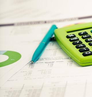 Close up of documents with a calculator and pen laying on top.