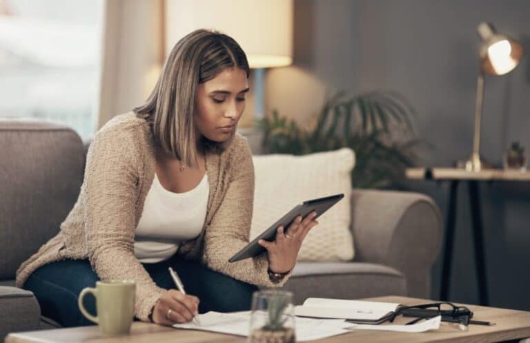 Shot of a young woman using a digital tablet while going through paperwork at home