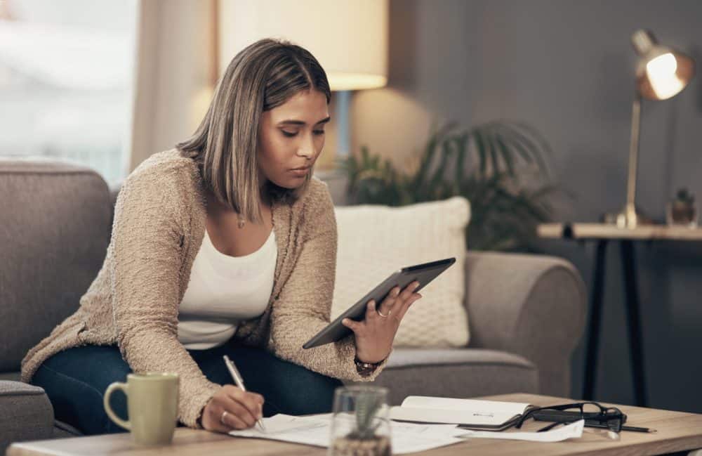 Shot of a young woman using a digital tablet while going through paperwork at home