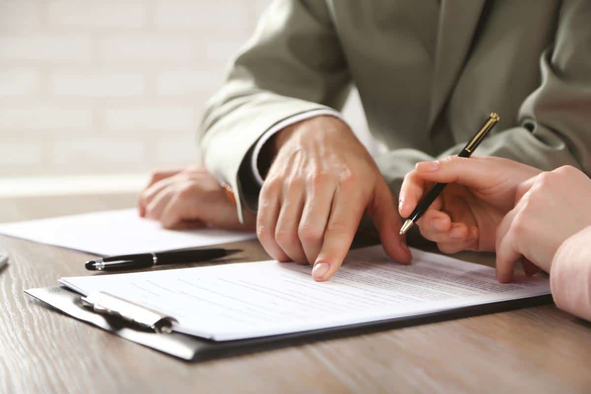 Close up of one employee signing contracts as the other points to details.