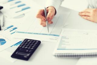 Close up of a woman working on documents with a calculator and pens lying around